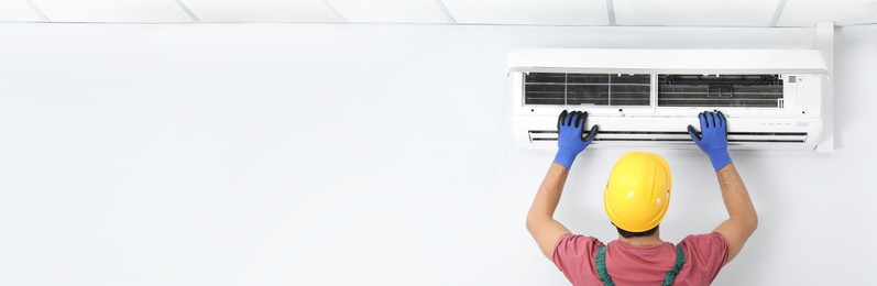 Male technician checking air conditioner indoors, space for text. Banner design