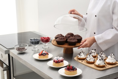 Photo of Female chef with pastries at table in kitchen, closeup