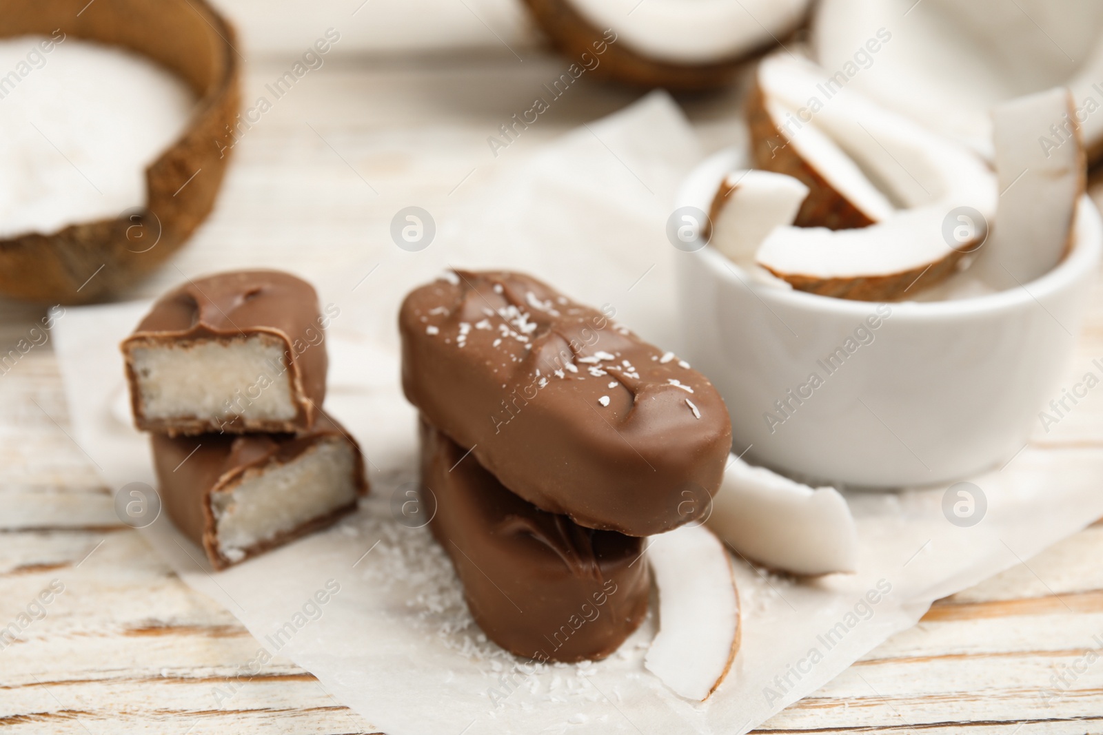 Photo of Delicious milk chocolate candy bars with coconut filling on white wooden table, closeup