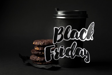 Photo of Takeaway paper coffee cup with phrase Black Friday and cookies against dark background