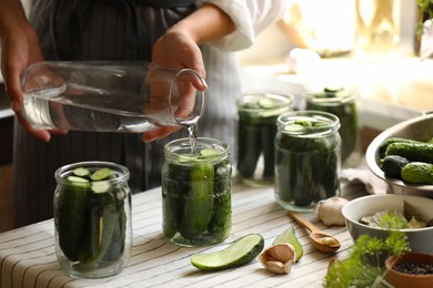 Photo of Woman pouring water into jar with canning cucumbers in kitchen, closeup