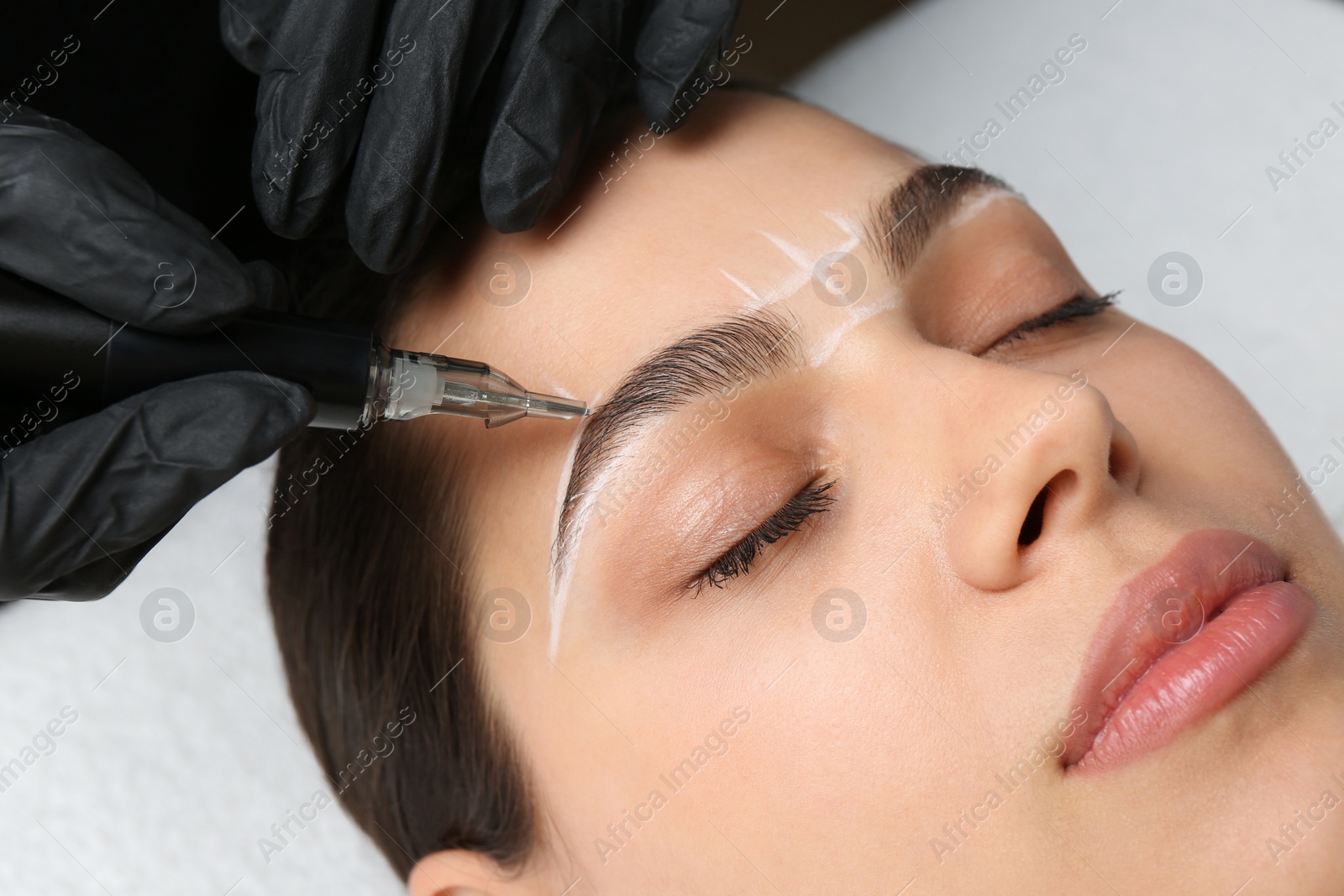 Photo of Beautician making permanent eyebrow makeup to young woman, closeup