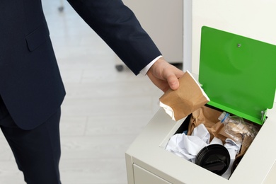 Photo of Man putting used paper cup into trash bin in office, closeup. Waste recycling
