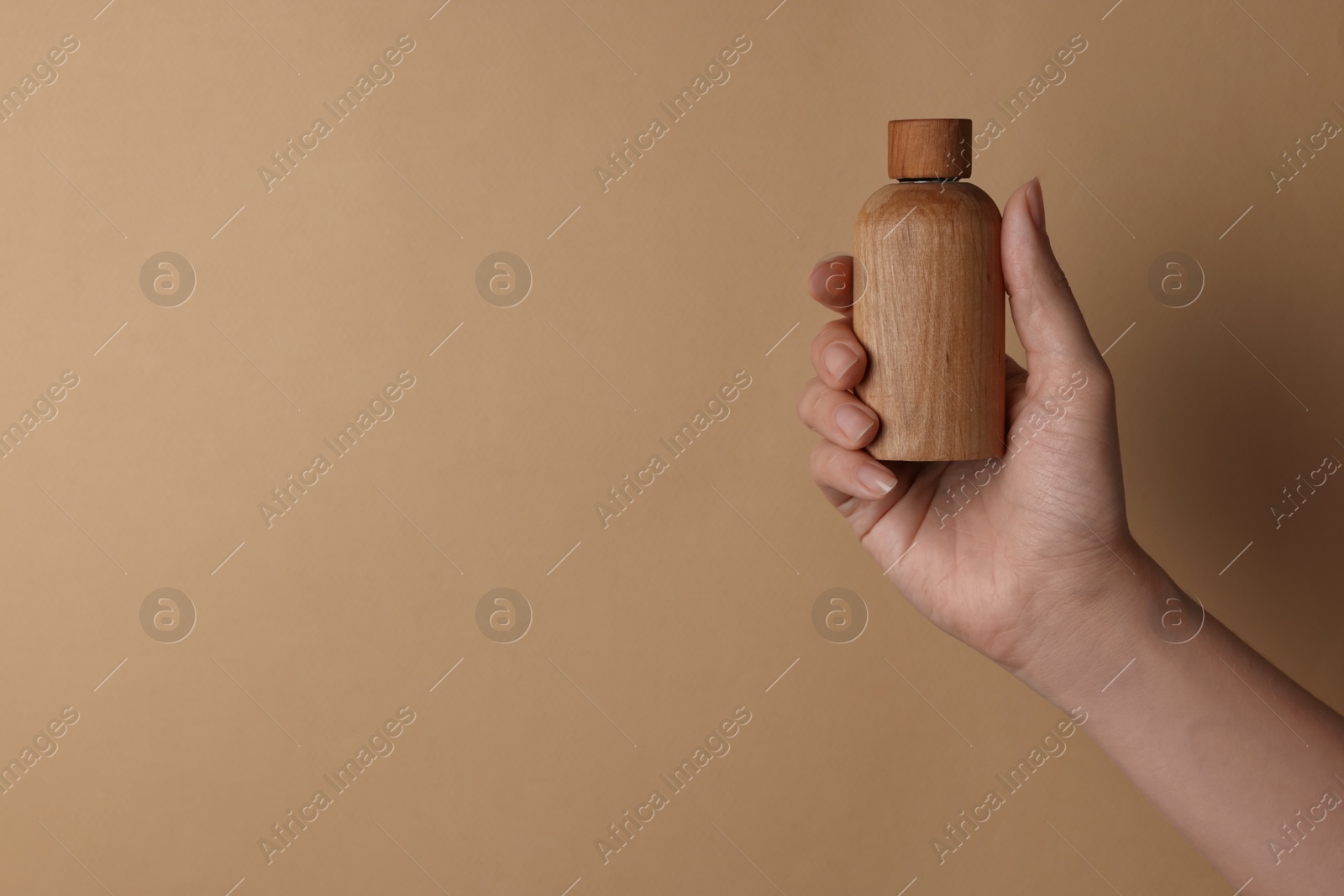 Photo of Woman holding bottle of cosmetic product on beige background, closeup. Space for text