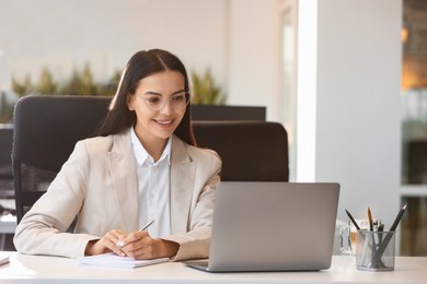 Photo of Happy woman using modern laptop at white desk in office