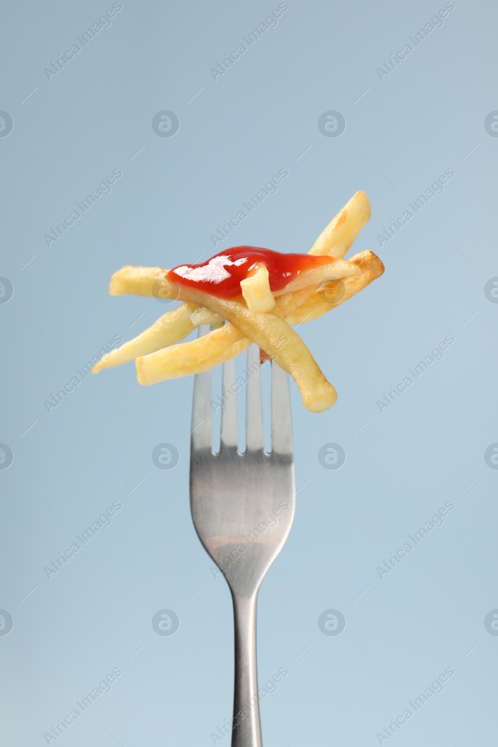 Photo of Fork with tasty french fries against light blue background, closeup