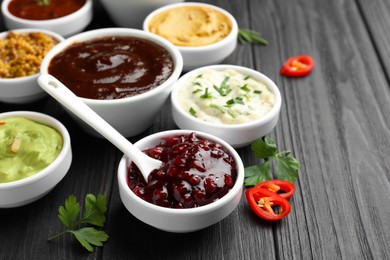 Photo of Different tasty sauces in bowls, parsley and chili pepper on black wooden table, closeup
