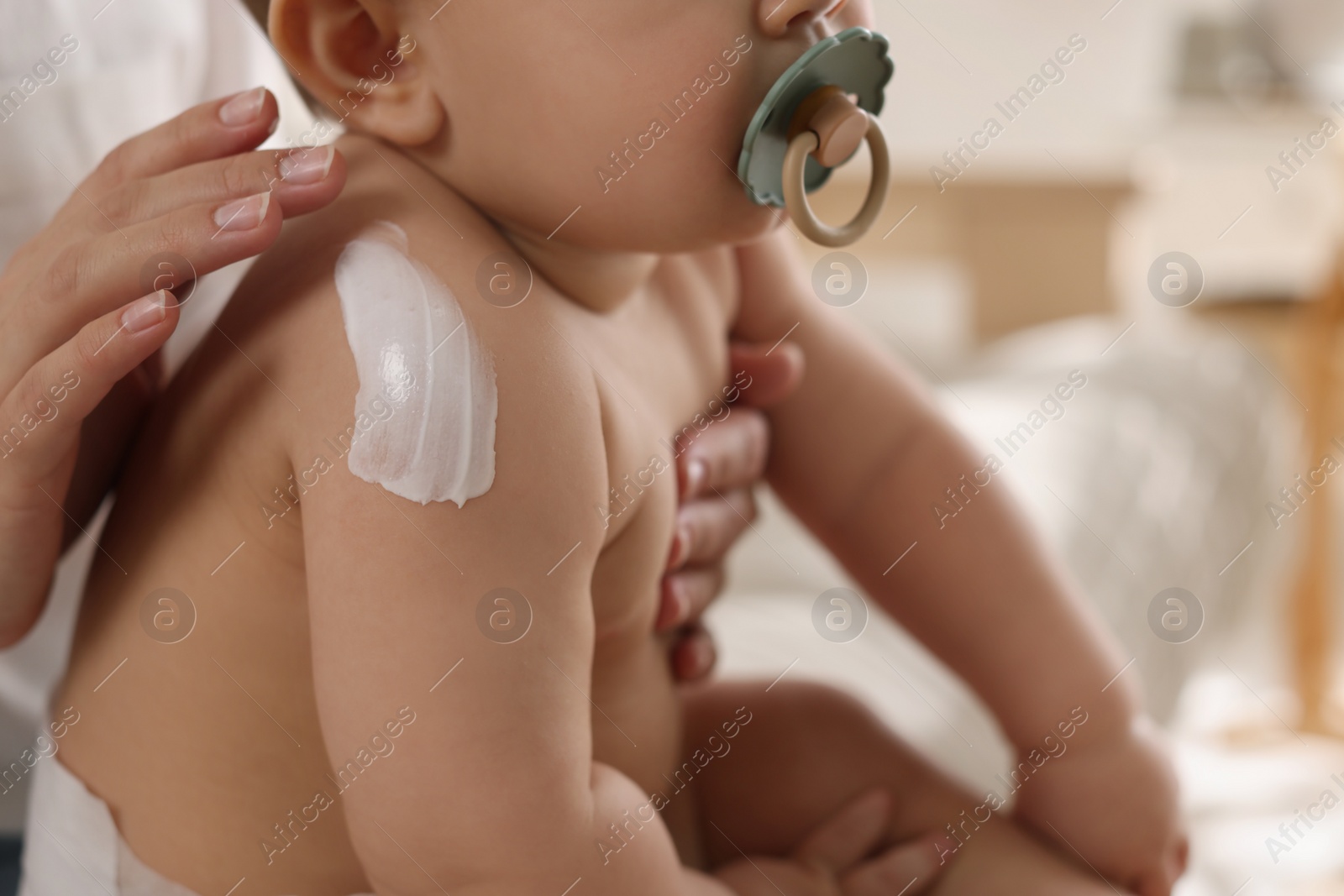 Photo of Mother applying body cream on her little baby at home, closeup