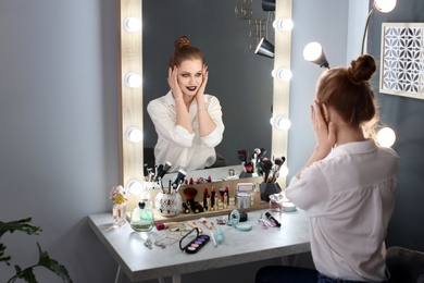 Photo of Beautiful young woman with makeup made by professional artist in dressing room