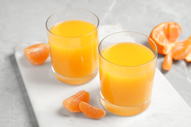 Glasses of fresh tangerine juice and fruits on light table