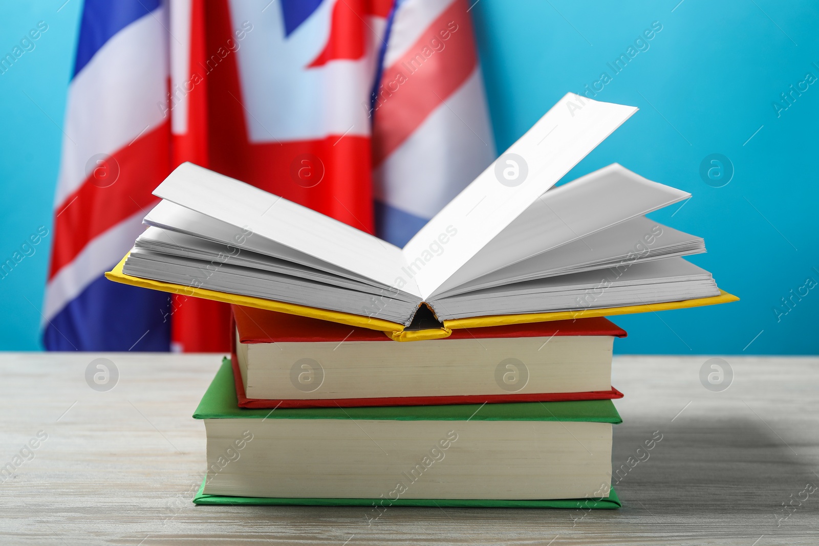 Photo of Learning foreign language. Different books on wooden table near flag of United Kingdom