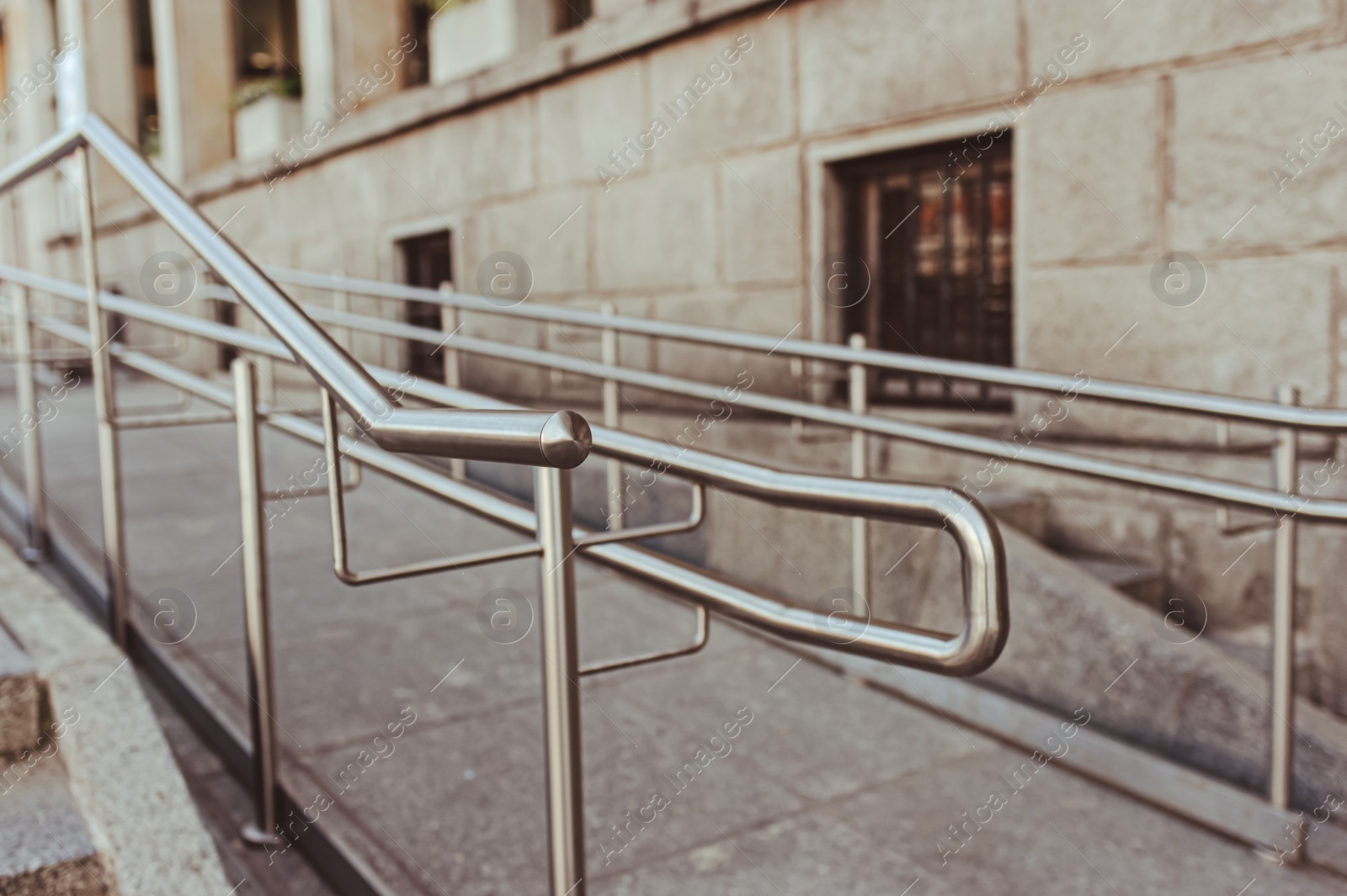 Photo of Tiled ramp with shiny metal railings outdoors