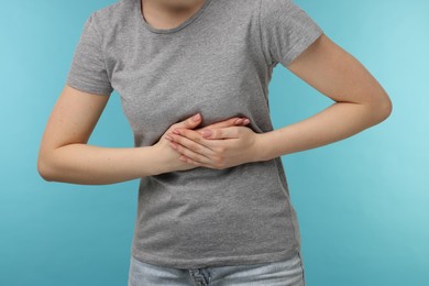 Photo of Woman suffering from stomach pain on light blue background, closeup