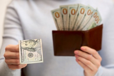 Photo of Woman giving 100 dollar bill and holding brown leather wallet with banknotes, closeup. Money exchange