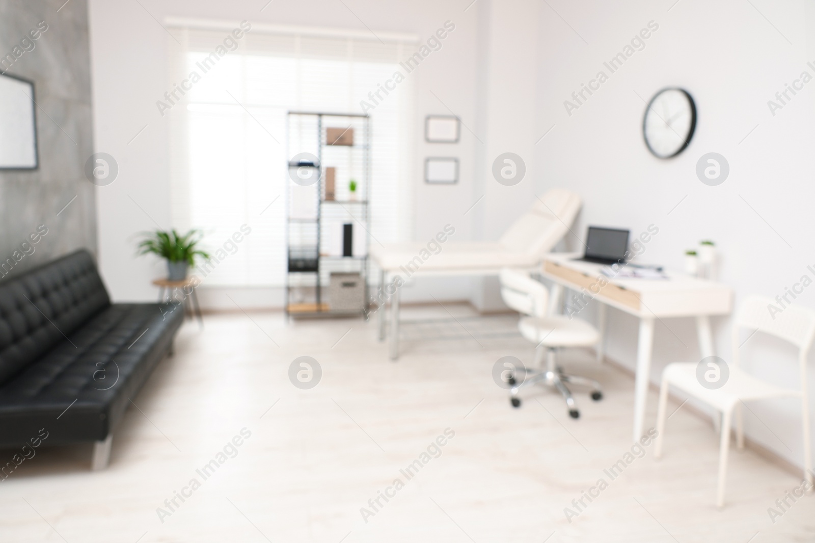 Photo of Blurred view of modern medical office with doctor's workplace and examination table in clinic