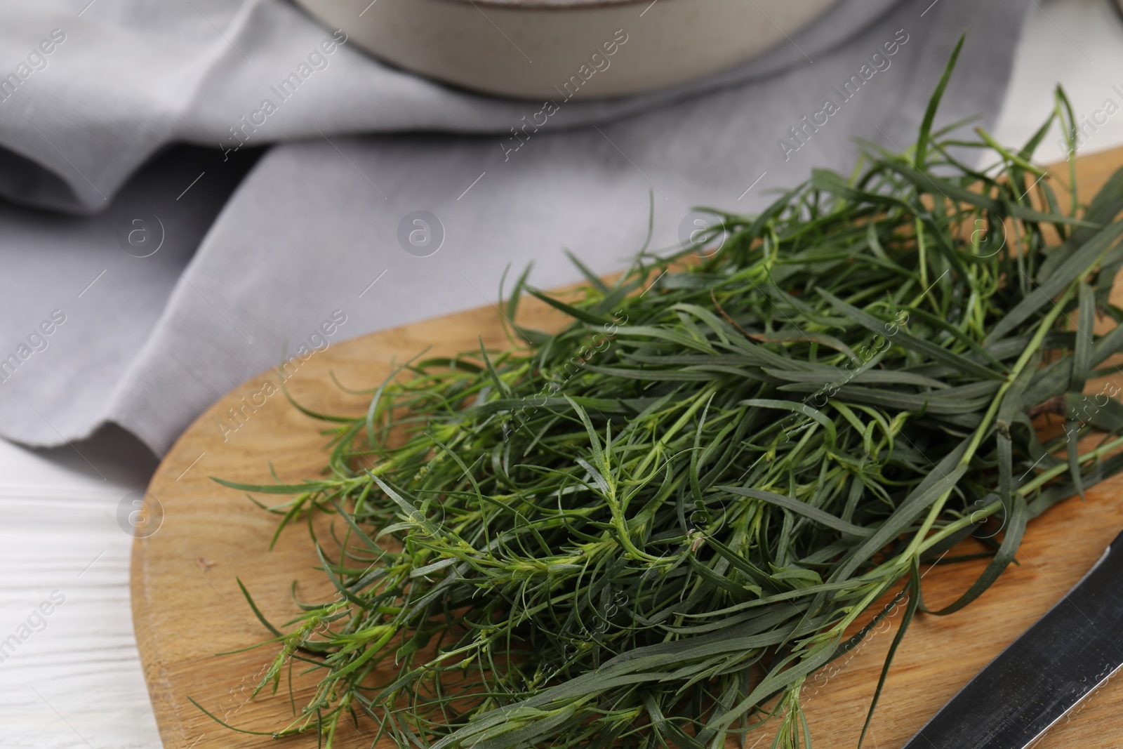 Photo of Fresh tarragon sprigs and knife on white wooden table, closeup