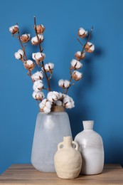 Photo of Vases and cotton branches on wooden table against light blue background