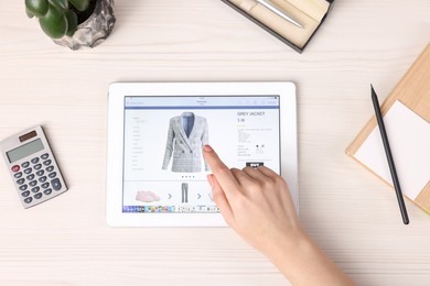 Woman with tablet shopping online at white wooden table, top view