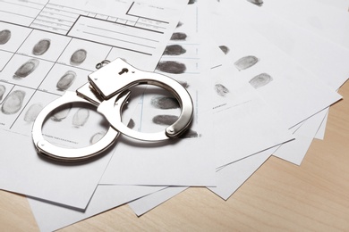 Photo of Police handcuffs and criminal fingerprints card on wooden background, space for text