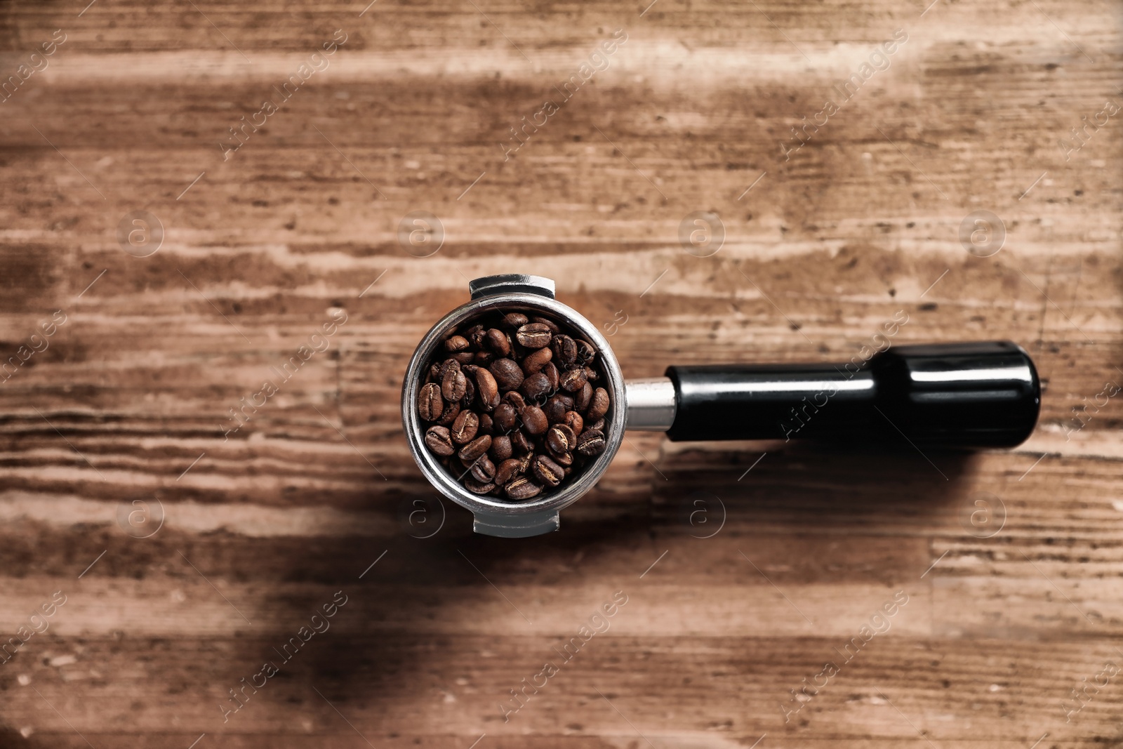Photo of Portafilter with roasted coffee beans on wooden table, top view