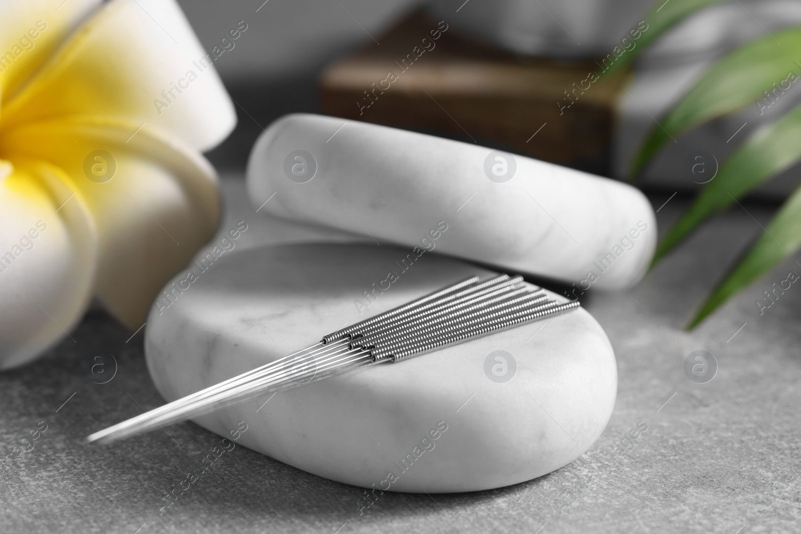 Photo of Stones with acupuncture needles and lily flower on grey table, closeup