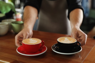 Photo of Barista putting cups of coffee on wooden table, closeup. Space for text