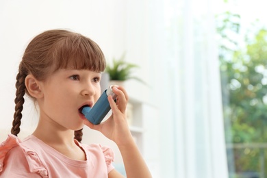 Photo of Little girl using asthma inhaler on blurred background