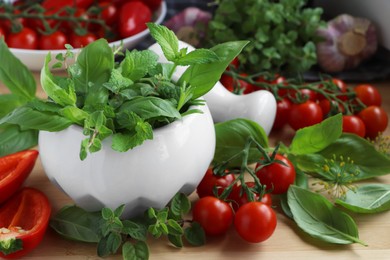 Photo of Mortar with fresh herbs, pepper and cherry tomatoes on wooden table, closeup