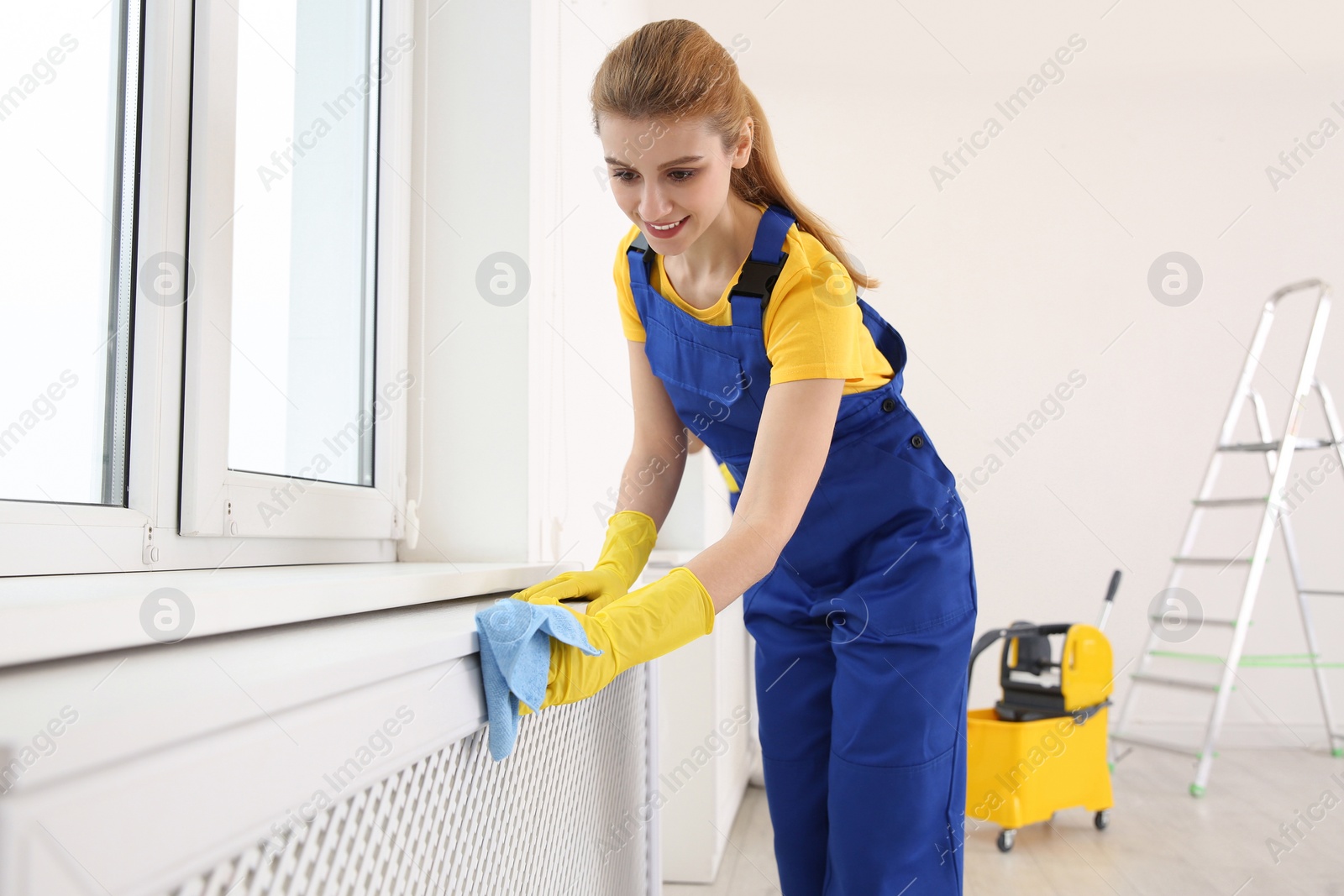 Photo of Professional young janitor cleaning windowsill in room