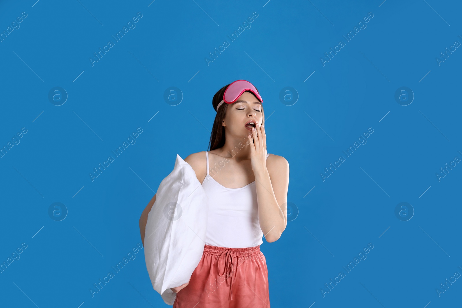 Photo of Young woman with pillow and sleep mask on blue background