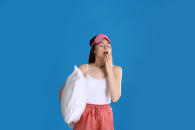 Young woman with pillow and sleep mask on blue background