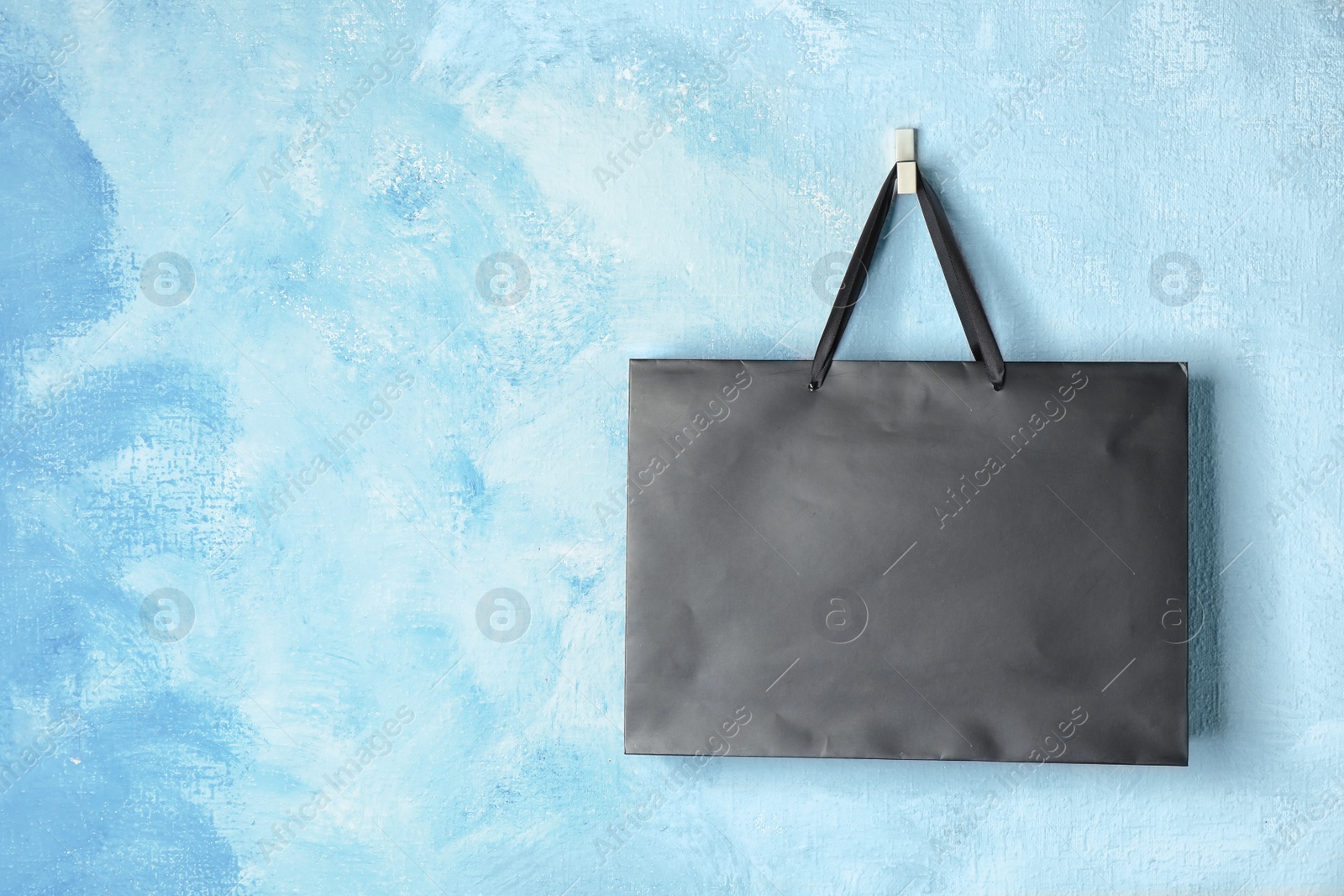 Photo of Paper shopping bag with handles hanging on color wall. Mock up for design