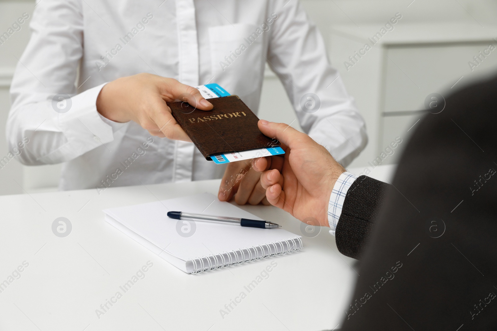 Photo of Manager giving passport and ticket to man at desk in travel agency office, closeup