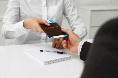 Manager giving passport and ticket to man at desk in travel agency office, closeup