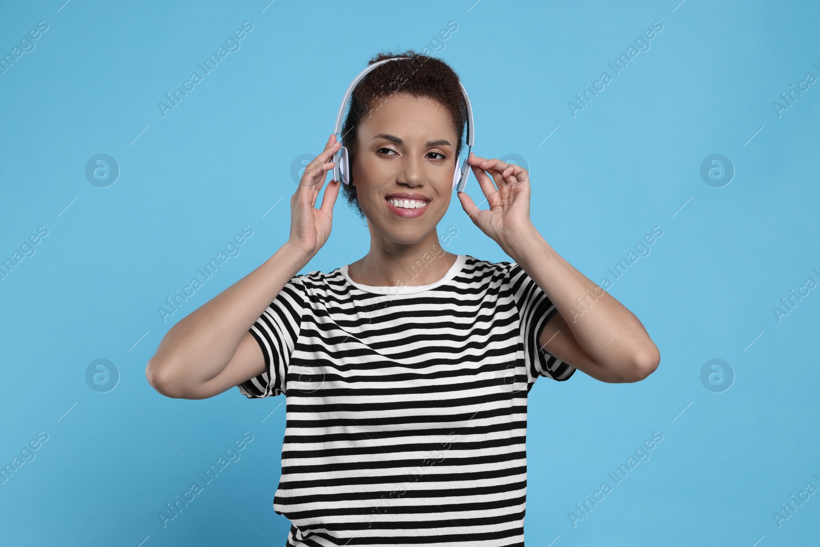 Photo of Happy young woman in headphones dancing on light blue background