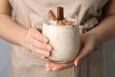 Woman holding glass of delicious rice pudding with cinnamon and hazelnuts, closeup