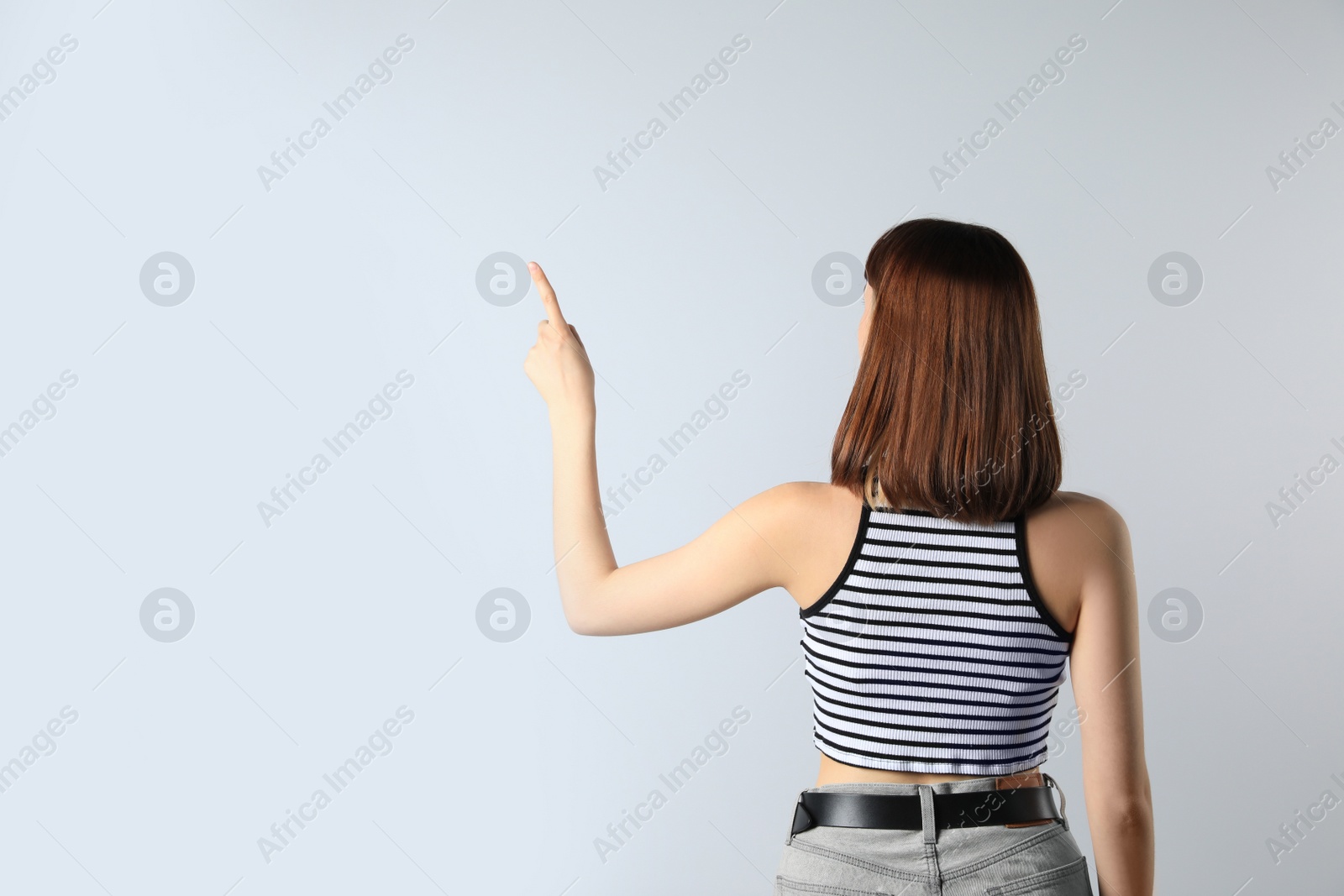 Photo of Young girl pointing on white background, back view. Space for text