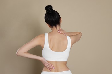 Woman suffering from pain in back on beige background