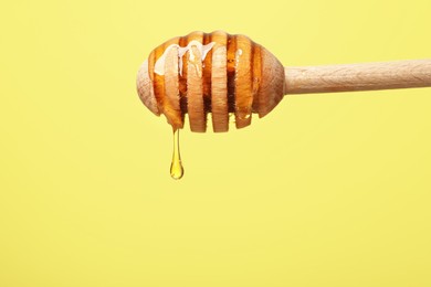 Photo of Delicious honey flowing down from dipper against yellow background, closeup. Space for text