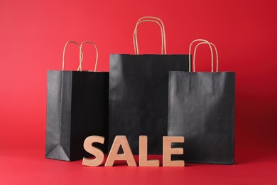 Word Sale made of wooden letters and shopping bags on red background. Black Friday