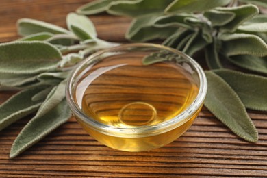 Photo of Bowl of essential sage oil and leaves on wooden table