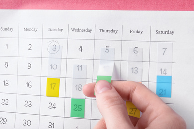 Woman marking date in calendar with sticker, closeup