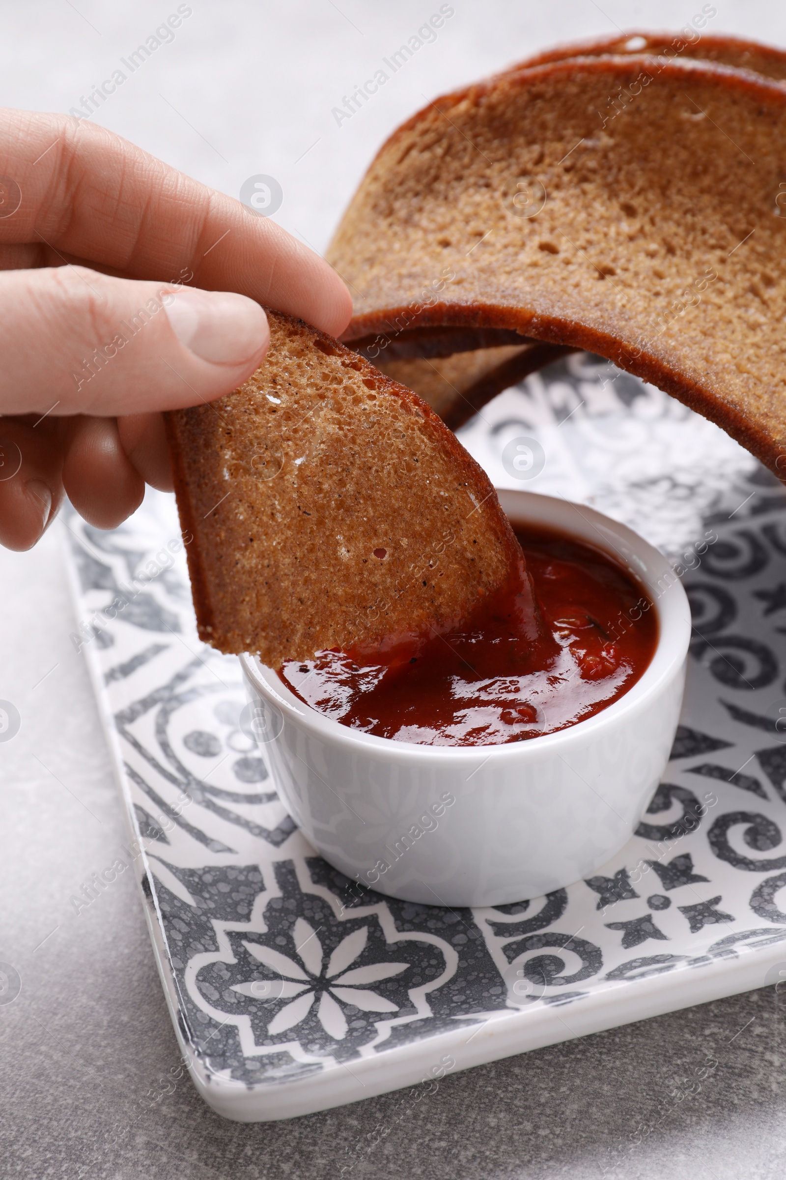 Photo of Woman dipping crispy rusk in sauce at light table, closeup