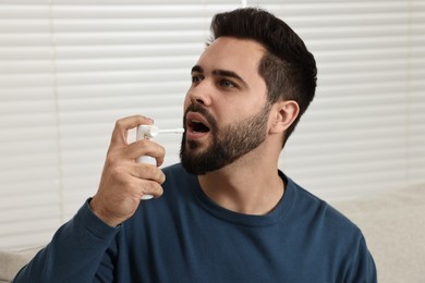 Photo of Young man using throat spray at home