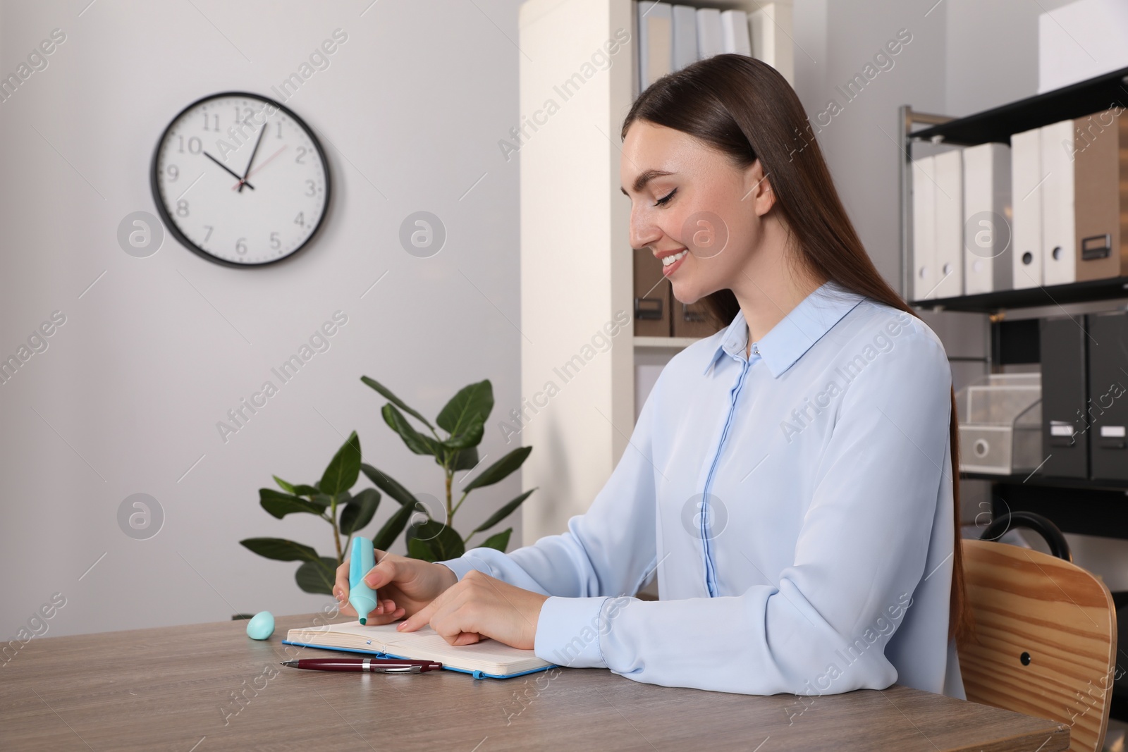 Photo of Happy woman taking notes at wooden table in office, space for text