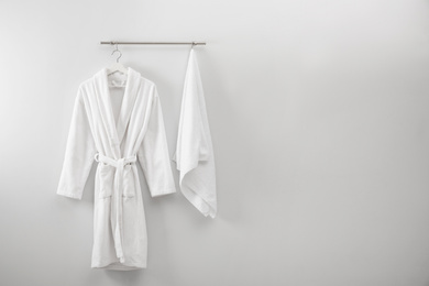 Photo of Hanger with clean bathrobe and towel on light wall. Space for text