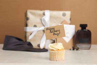 Photo of Happy Father's Day. Tasty cupcake with greetings in front of presents on light marble table, closeup