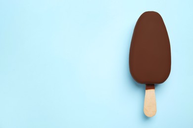 Photo of Ice cream glazed in chocolate on light blue background, top view. Space for text