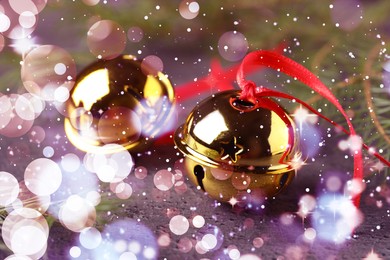 Golden sleigh bells and fir branches on table, closeup. Bokeh effect