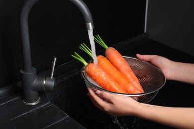 Photo of Woman washing fresh ripe juicy carrots under tap water in sink, closeup